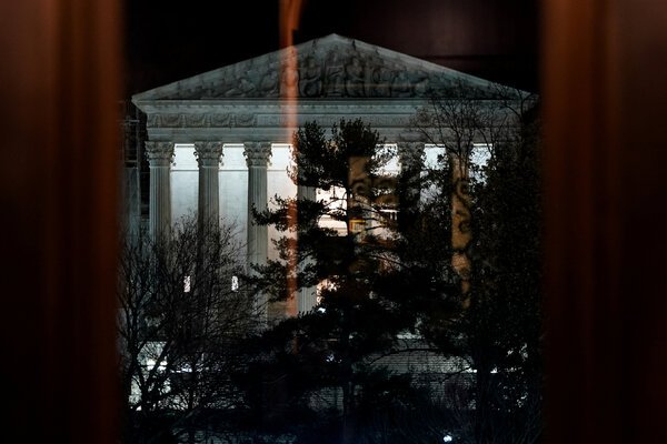 A view of the Supreme Court structure under dark skies with the portico lighted.